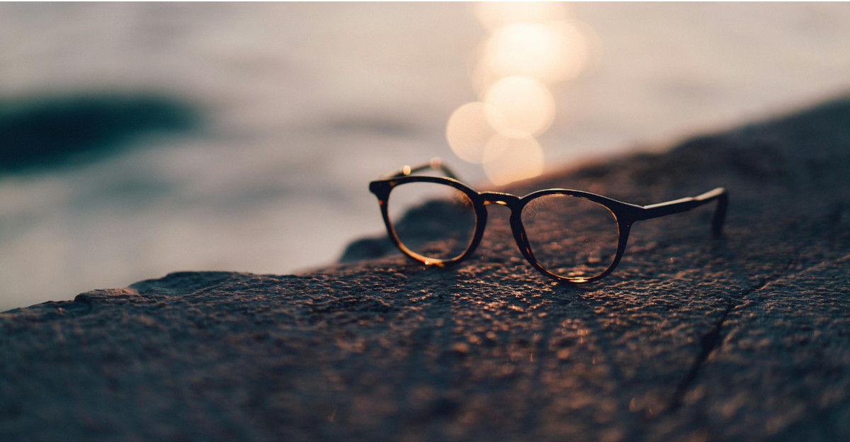 Nahaufnahme einer schwarz gerahmten Sonnenbrille mit klarem Glas in der Nähe eines Gewässers